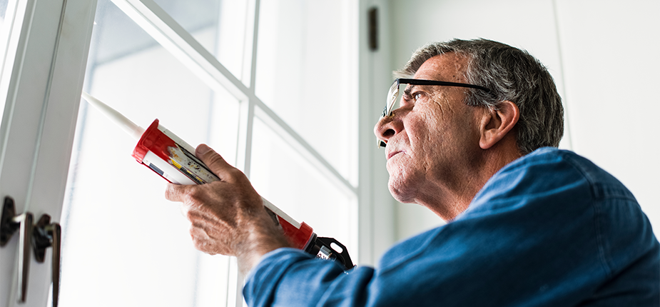 Homeowner sealing their windows against leaks, one of the energy saving home maintenance tips provided by Consumers Energy